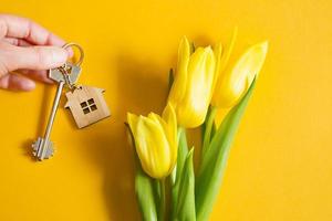 House keys in hand on yellow background and spring tulips. Building, design, project, moving to new home, mortgage, rent and purchase real estate, summer offer from the agent. Copy space photo