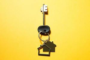 Key chain in the shape of wooden house with key on a yellow background. Building, design, project, moving to new home, mortgage, rent and purchase real estate. Copy space photo