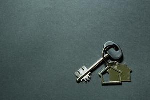 Key chain in the shape of house with key on a black background. Building, design, project, moving to new home, mortgage, deposit, rent and purchase real estate. Copy space photo