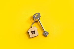 Key chain in the shape of wooden house with key on a yellow background. Building, design, project, moving to new home, mortgage, rent and purchase real estate. Copy space photo