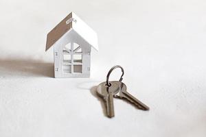 White wooden house symbol and keys on a gray background. Cottage construction concept, layout and design, architectural plan, moving to a new house, realtor, ready business. Space for text, flatly photo