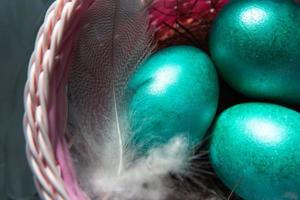 Colorful painted marble shiny Easter eggs in a basket with delicate feathers close-up. Nest with straw - Easter decoration on the table photo