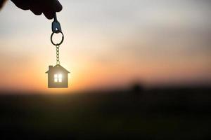 Silhouette of a house figure with a key, a pen with a keychain on the background of the sunset. They dream of a house, building, moving to a new house, mortgages, renting and buying real estate.