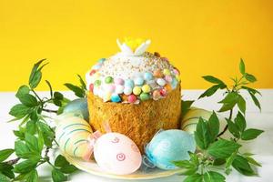 Easter cake with painted eggs on a platter in a white table. Traditional festive food. Yellow background photo