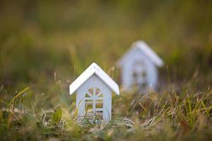 Figures of small white wooden houses on the grass close-up. The cottage is in a rural location and village, building, project, moving , mortgage, rent and purchase real estate. Copy space photo