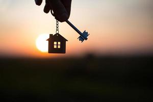 Silhouette of a house figure with a key, a pen with a keychain on the background of the sunset. They dream of a house, building, moving to a new house, mortgages, renting and buying real estate photo