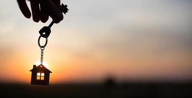 Silhouette of a house figure with a key, a pen with a keychain on the background of the sunset. They dream of a house, building, moving to a new house, mortgages, renting and buying real estate