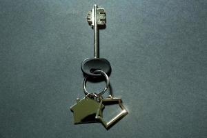 Key chain in the shape of house with key on a black background. Building, design, project, moving to new home, mortgage, deposit, rent and purchase real estate. Copy space photo