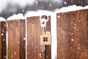 Key to the house on a wooden fence in winter in the snow. A gift for New Year, Christmas. Building, design, project, moving to new house, mortgage, rent and purchase real estate. Copy space photo