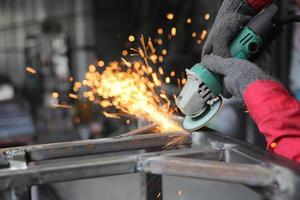 soldador utilizó piedra de moler sobre acero en fábrica con chispas, proceso de soldadura en el taller industrial, manos con instrumento en marco. foto