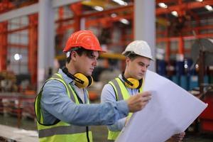 Men industrial engineer wearing a safety helmet while standing in a heavy industrial factory. The Maintenance looking of working at industrial machinery and check security system setup in factory. photo