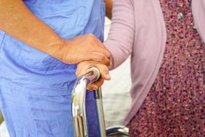 cuidador ayuda a una anciana asiática con discapacidad a caminar con un andador en un hospital de enfermería, concepto médico. foto