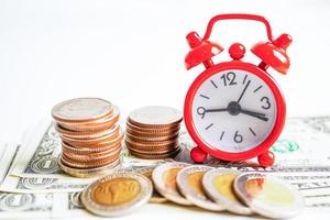 Alarm clock with coins on US dollar banknotes, finance installment loan time. photo