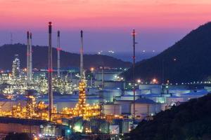 A large oil refinery with many crude oil storage tanks at sunset.