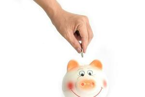 Hands putting coin into a piggy bank on white background. Saving and investing money concept. photo