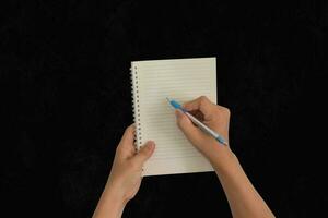 Hand holding pen, with a blank notes over blackboard background. Design concept photo