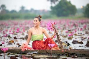 Young Asian women in Traditional dress in the boat and pink lotus flowers in the pond.Beautiful girls in traditional costume.Thai girl in retro Thai dress, Thai girl in traditional dress costume photo