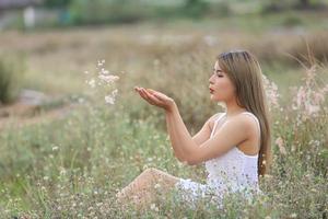 Beautiful Young Woman sitting on the field in green grass and blowing dandelion. Outdoors. Enjoy Nature. Healthy Smiling Girl on spring lawn. Allergy free concept. Freedom photo