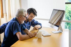 adult man teaching elderly man to using computer at home.