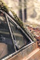 viejo coche abandonado y oxidado en un bosque cubierto de musgo foto