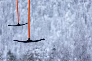 Two t-bar skiing lift poles against blurred snow forest.
