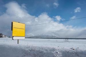 Yellow traffic signboard on snow covered roadside photo