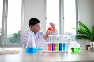 niño pequeño mezcla productos químicos en vasos de precipitados. niños con tubos de ensayo haciendo experimentos en el laboratorio escolar. foto