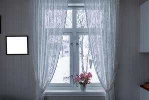 Pink flower on window sill with curtain and picture frame on winter season photo