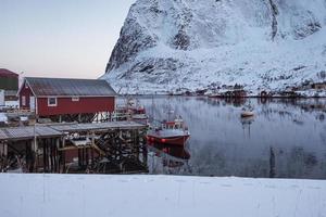 barco de pesca anclado en el muelle con pueblo rojo en invierno en lofoten foto