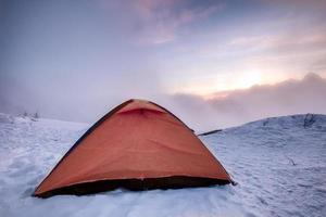 Camping orange tent on snowy hill in morning