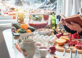 hombre leyendo un libro con la preparación de alimentos en la mesa de comedor con nieve en el pueblo foto