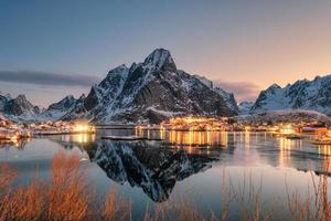 Fishing village illumination with mountain range reflection on coastline at dawn photo