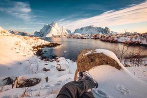 Legs of traveler relaxing in snow covered reine town on coastline at Lofoten islands
