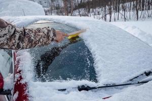 Hand using brush sweeping snow on car windscreen photo