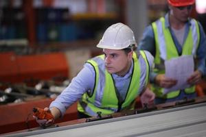 el capataz de los trabajadores de la industria o el trabajo de los trabajadores en el sitio de la fábrica revisan la máquina o los productos en el sitio. ingeniero o técnico revisando material o máquina en planta. industrial y fábrica. foto