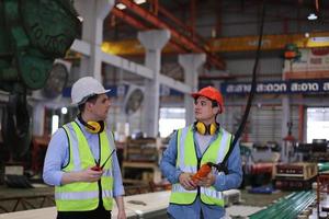 Men industrial engineer wearing a safety helmet while standing in a heavy industrial factory. The Maintenance looking of working at industrial machinery and check security system setup in factory. photo