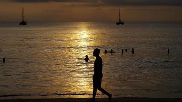 beau coucher de soleil avec des silhouettes de personnes profitant de l'océan. video