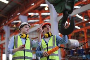 Men industrial engineer wearing a safety helmet while standing in a heavy industrial factory. The Maintenance looking of working at industrial machinery and check security system setup in factory. photo