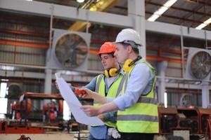 Men industrial engineer wearing a safety helmet while standing in a heavy industrial factory. The Maintenance looking of working at industrial machinery and check security system setup in factory. photo