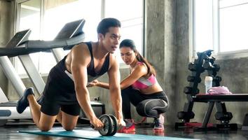 pareja atleta deportistas haciendo ejercicio con rueda de rodillos abs para fortalecer su músculo abdominal en el gimnasio. foto