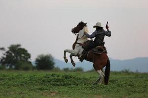 vaquero montando a caballo con la mano sosteniendo un arma contra el fondo del atardecer. foto