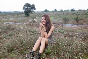 hermosa mujer joven sentada en el campo de hierba verde y soplando diente de león. al aire libre. disfruta de la naturaleza. niña sonriente saludable en el césped de primavera. concepto libre de alergias. libertad foto