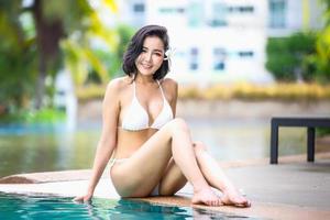 mujer en bikini blanco bronceándose junto a la piscina foto