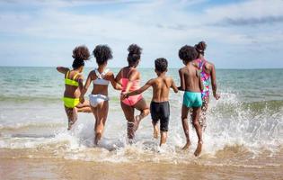 Kids playing running on sand at the beach, A group of children holding hands in a row on the beach in summer, rear view against sea and blue sky photo