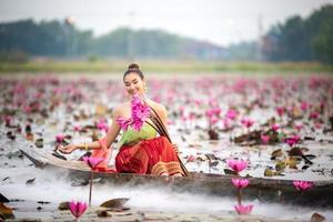 Young Asian women in Traditional dress in the boat and pink lotus flowers in the pond.Beautiful girls in traditional costume.Thai girl in retro Thai dress, Thai girl in traditional dress costume photo