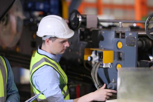 Men industrial engineer wearing a safety helmet while standing in a heavy industrial factory. The Maintenance looking of working at industrial machinery and check security system setup in factory. photo