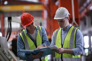 ingeniero industrial masculino con casco de seguridad mientras está de pie en una fábrica industrial pesada. el mantenimiento que busca trabajar en maquinaria industrial y verificar la configuración del sistema de seguridad en fábrica. foto