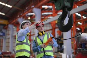 Men industrial engineer wearing a safety helmet while standing in a heavy industrial factory. The Maintenance looking of working at industrial machinery and check security system setup in factory. photo