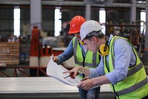 Men industrial engineer wearing a safety helmet while standing in a heavy industrial factory. The Maintenance looking of working at industrial machinery and check security system setup in factory. photo