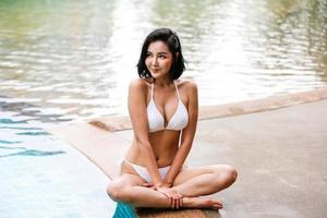 mujer joven disfrutando y relajándose junto a la piscina. modelo de chica joven delgada en bikini blanco junto a la piscina. foto